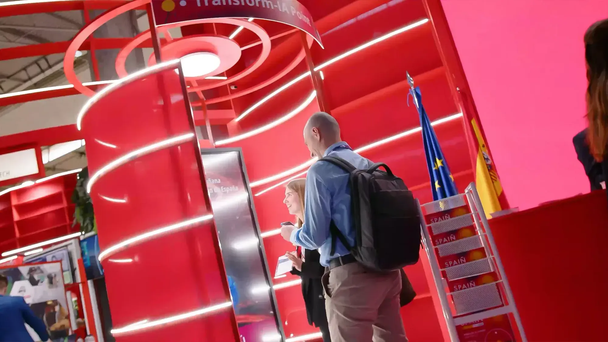 Visitors approaching a curved red structure with rings of LED light on a trade fair stand